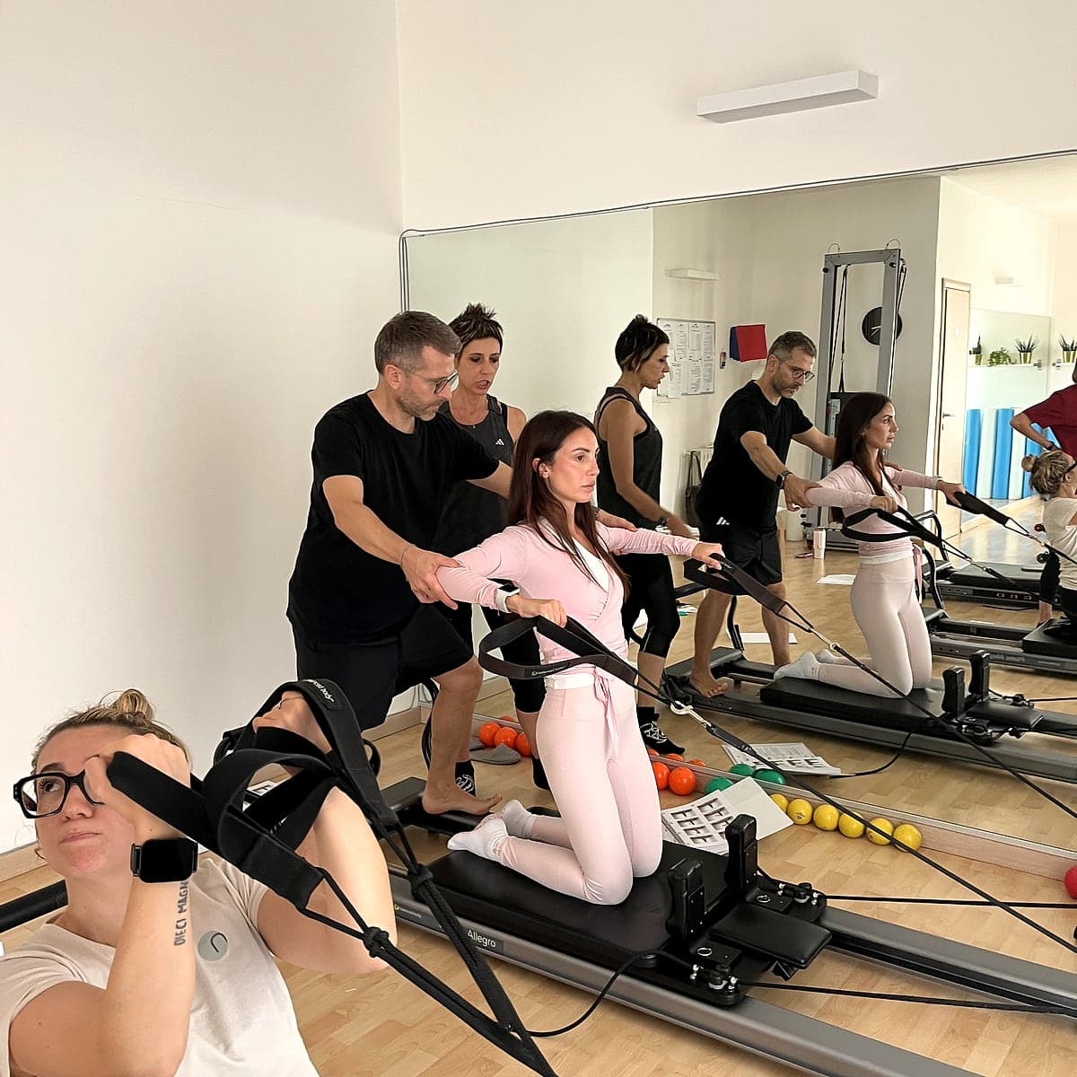 Vincenzo guida una corsista sul reformer durante una lezione di gruppo.